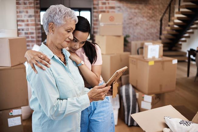 This photograph captures an intimate and nostalgic moment between two women, likely an older woman and a younger family member, as they pack up their home.